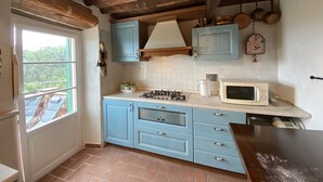 A kitchen with blue cabinets, a white tiled backsplash, a wooden ceiling, and a window with a view of greenery. - Charming house in old stone wall village (Fibbiano)