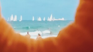 Ein Strandbild, das durch einen runden Rahmen betrachtet wird, mit Wellen und einigen Personen.