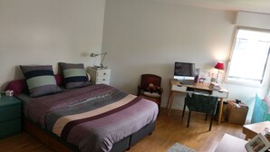 Ett sovrum med en säng, ett skrivbord, en stol och ett fönster.