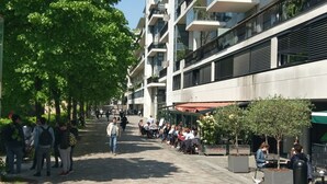 Ett stenbelagt område för fotgängare med moderna byggnader, uteserveringar och träd.