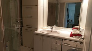 Ett modernt badrum med en duschkabin i glas, ett vitt handfat med spegel och en tvättmaskin från Siemens.
