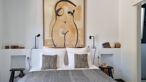 A bedroom with a bed, pillows, a wall art piece, bedside tables, and a door leading to another room.