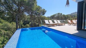 A clear blue pool with lounge chairs and a deck overlooking a forested area.