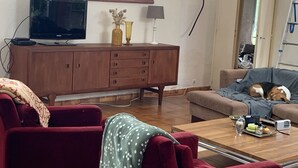 A living room with a red sofa, a coffee table with snacks, a TV on a wooden cabinet, and a painting on the wall.