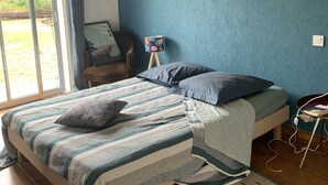 A bedroom with a bed, pillows, a rug, a chair, a small table, and a painting on the wall.