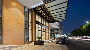 Een modern gebouw met een grote glazen gevel, een bord waarop staat 'Binnenkort geopend' en een zwarte auto die ervoor geparkeerd staat.