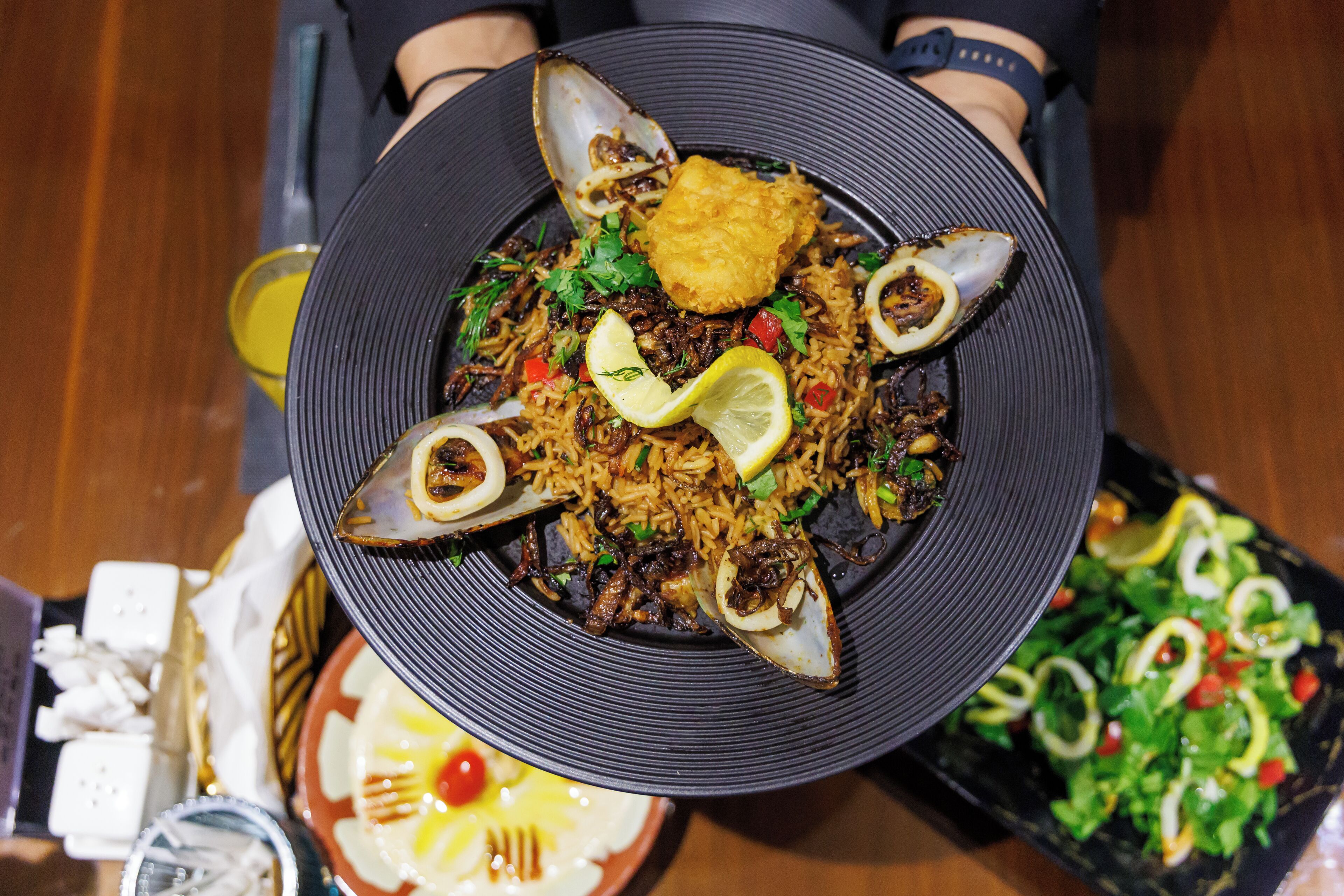 Een bord met zeevruchtenrijst, citroenpartjes en een salade.