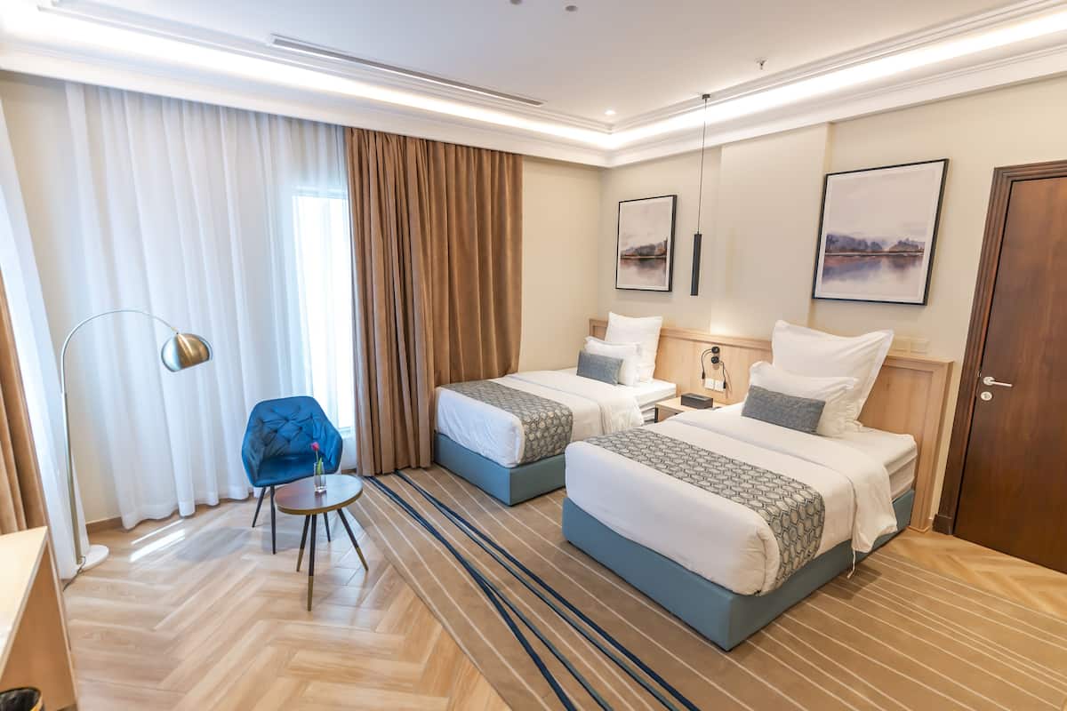 A hotel room with two beds, a desk, a chair, and a large window with curtains.