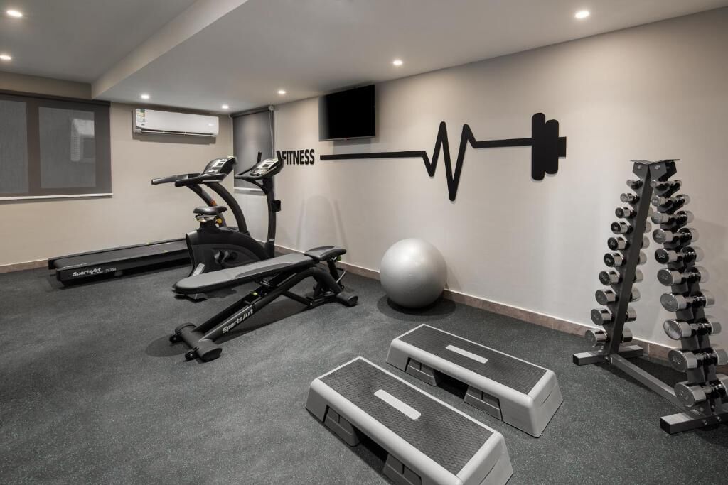 A gym with treadmills, a stationary bike, a rowing machine, a medicine ball, stepper machines, and a rack of dumbbells.