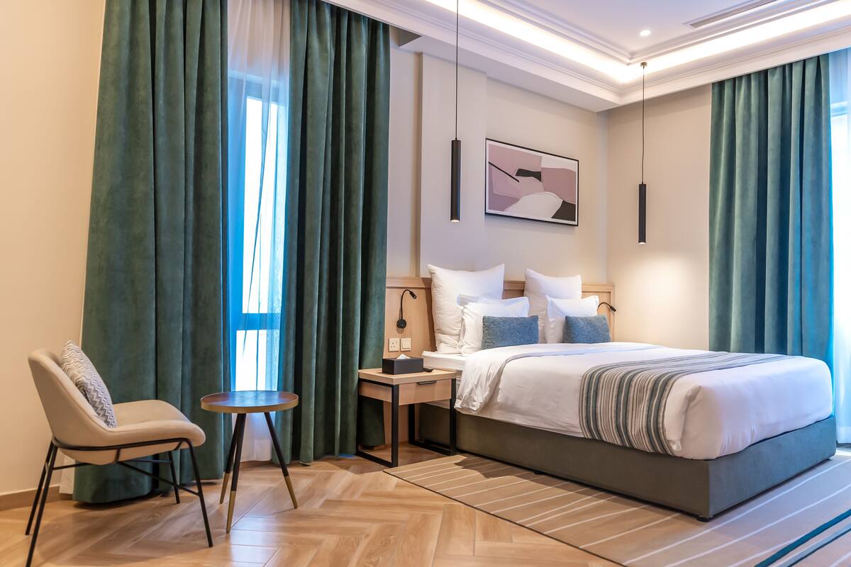 A modern hotel room with a large bed, a chair, a small table, and a nightstand.
