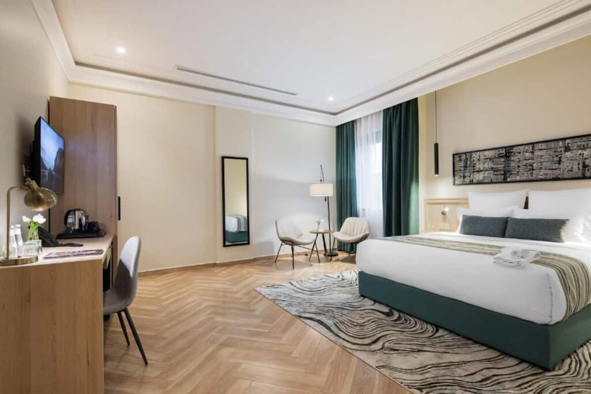A hotel room with a large bed, a desk with a TV, a chair, a lamp, and a painting on the wall.