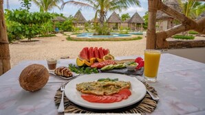 A table with a plate of food, a glass of juice, and a coconut. - HABER HOTEL & SPA (Matemwe)