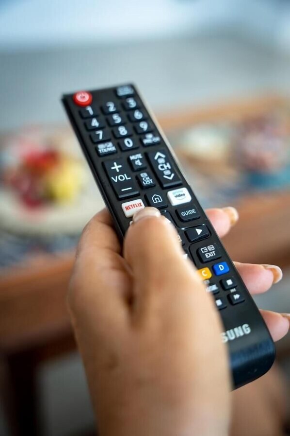 Una mano sostiene un control remoto con teclado numérico y varios botones, incluyendo un botón de Netflix.
