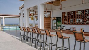 A bar area with wooden stools and a bar counter, a refrigerator, and a wall of liquor bottles. - HABER HOTEL & SPA (Matemwe)