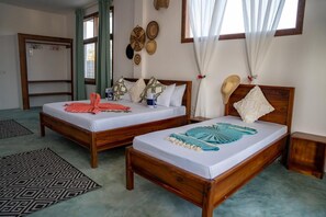 A double bed room with two wooden beds, a patterned rug, and a window with curtains. - HABER HOTEL & SPA (Matemwe)