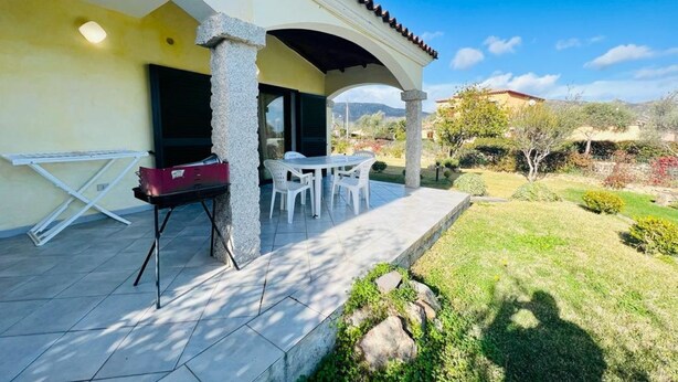 Eine Terrasse mit Tisch und Stühlen, ein überdachter Bereich und Blick auf die umliegende Landschaft.