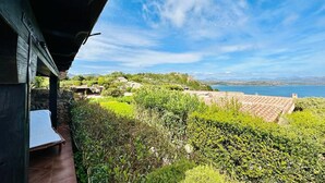 Une terrasse avec un lit, une végétation luxuriante et une vue sur la mer et les collines.