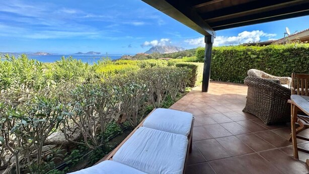 Une terrasse couverte avec vue sur la mer, une chaise longue et une table en osier.