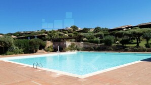 Une piscine rectangulaire, bordée d’une terrasse carrelée, entourée de verdure et avec des collines en arrière-plan.
