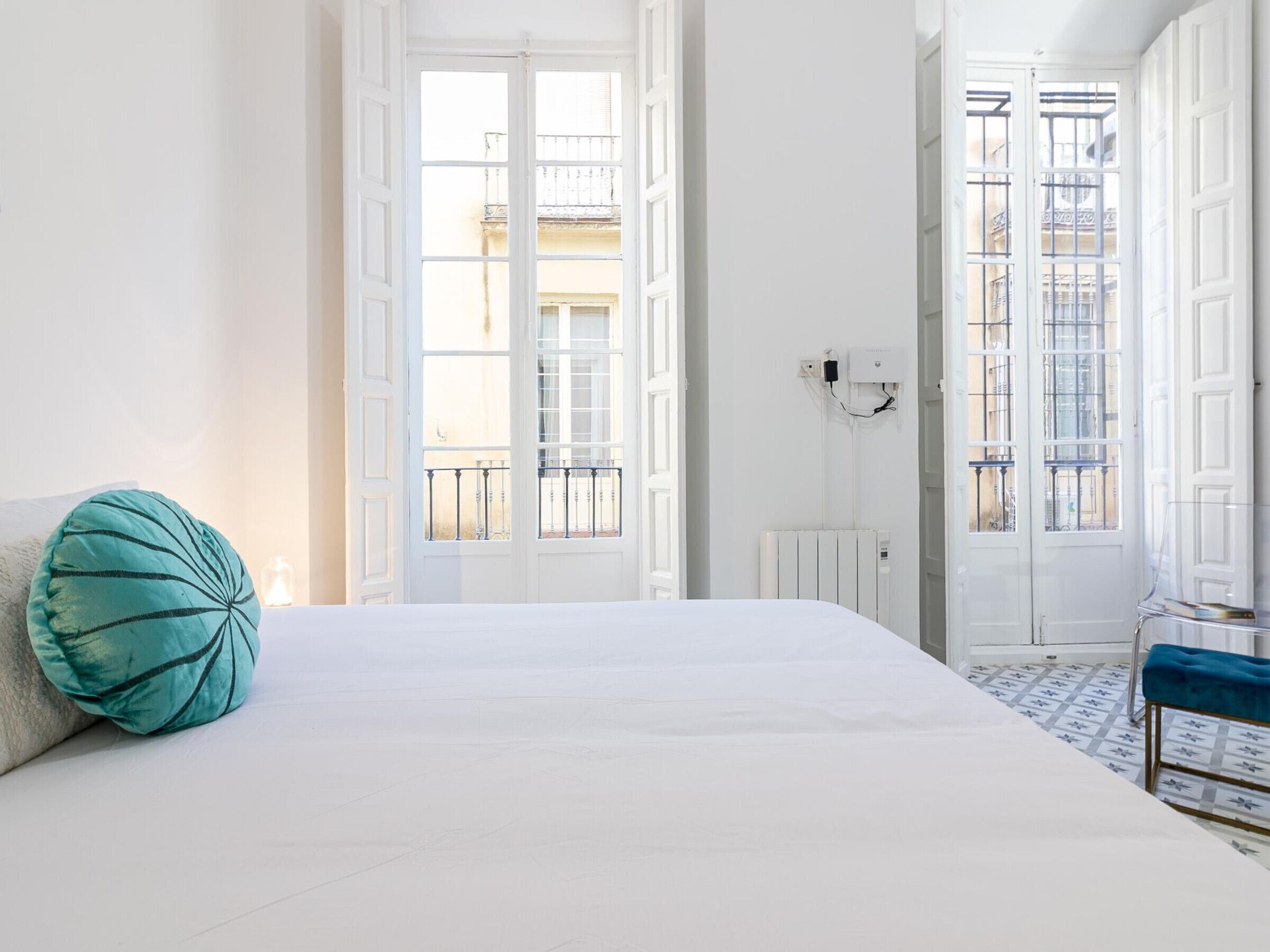 Een slaapkamer met een groot bed, een teal kussen, een radiator en uitzicht op het balkon.