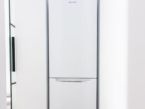 A white, modern refrigerator with a minimalist design, featuring a single control panel at the top and a lower compartment.