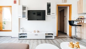 Una sala de estar moderna con un televisor de pantalla plana montado en la pared, un mueble blanco debajo y una zona de comedor con un taburete de bar.