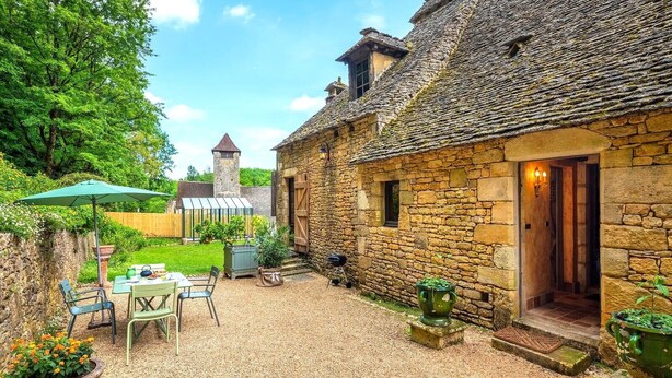 A stone building with a thatched roof, a small tower, and a patio area with outdoor seating and potted plants.
