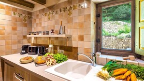 A kitchen with a large sink, a window with a view of greenery, and various kitchen appliances and fresh produce on the counter.