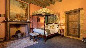 A traditional bedroom with a four-poster bed, a fireplace, and a stone wall.
