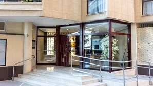 Una entrada moderna con puertas de vidrio, una escalera de metal y un muro de ladrillo.