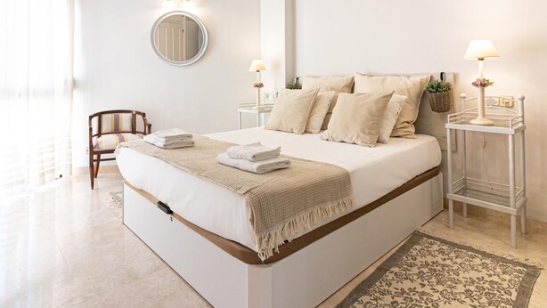 Un dormitorio amplio con una cama grande, mesitas de noche, un espejo y una lámpara colgante.