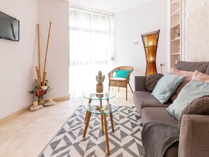 A living room with a sofa, a glass coffee table, a wicker chair, and a cactus plant.