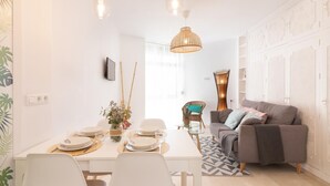 Una sala de estar moderna con comedor, que incluye un sofá, una mesa de comedor preparada para cuatro comensales y un televisor montado en la pared.