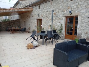 Une terrasse extérieure avec des murs en pierre, une table avec des chaises et un canapé en osier.
