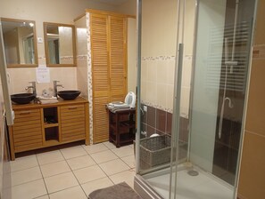 Une salle de bain avec un meuble-lavabo en bois, deux vasques, une douche en verre et un sol carrelé.