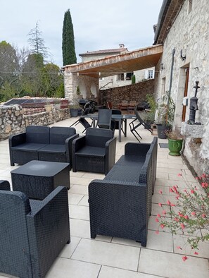 Une terrasse extérieure avec des meubles en osier, un mur en pierre et une pergola.