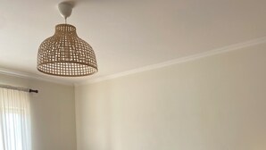 Une chambre à coucher avec un grand lit, une chaise, deux tables de chevet avec des lampes, une tête de lit en osier et un luminaire suspendu.