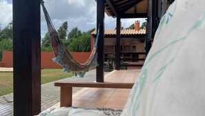 Un hamac sous une pergola en bois, un espace patio avec un banc, et une vue sur un bâtiment avec un toit en tuiles.