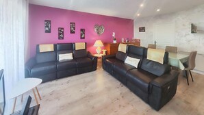 A living room with a purple wall, two black sofas with cushions, a small table with a lamp, and a dining area with chairs and a table. - Awesome home in Portiragnes (Portiragnes)