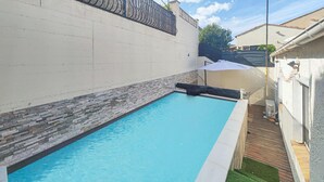 A rectangular swimming pool with a stone border, adjacent to a white wall and a wooden deck. - Awesome home in Portiragnes (Portiragnes)