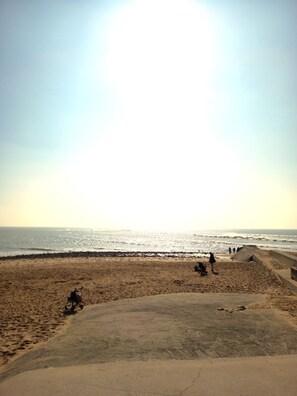A beach with a concrete area in the foreground, a sandy beach, and the ocean in the background.