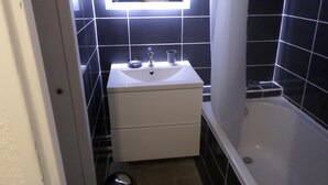 A bathroom with a white sink, mirror, and bathtub. - Studio Canet Plage (CANET PLAGE)