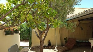 A patio area with a tree, a bench, a small table, and a wooden deck. - À 10 Minutes de la Plage, Petite Maison au Calme Avec Patio (Le Barcarès)