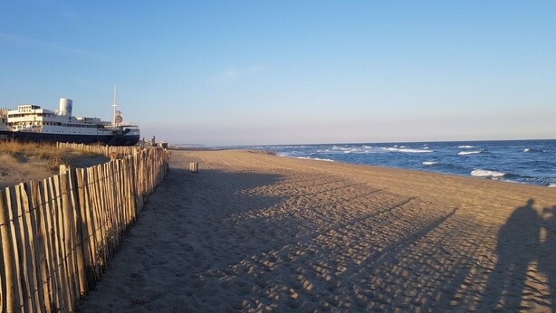 A sandy beach with a wooden fence and a boat docked on the left. - À 10 Minutes de la Plage, Petite Maison au Calme Avec Patio (Le Barcarès)