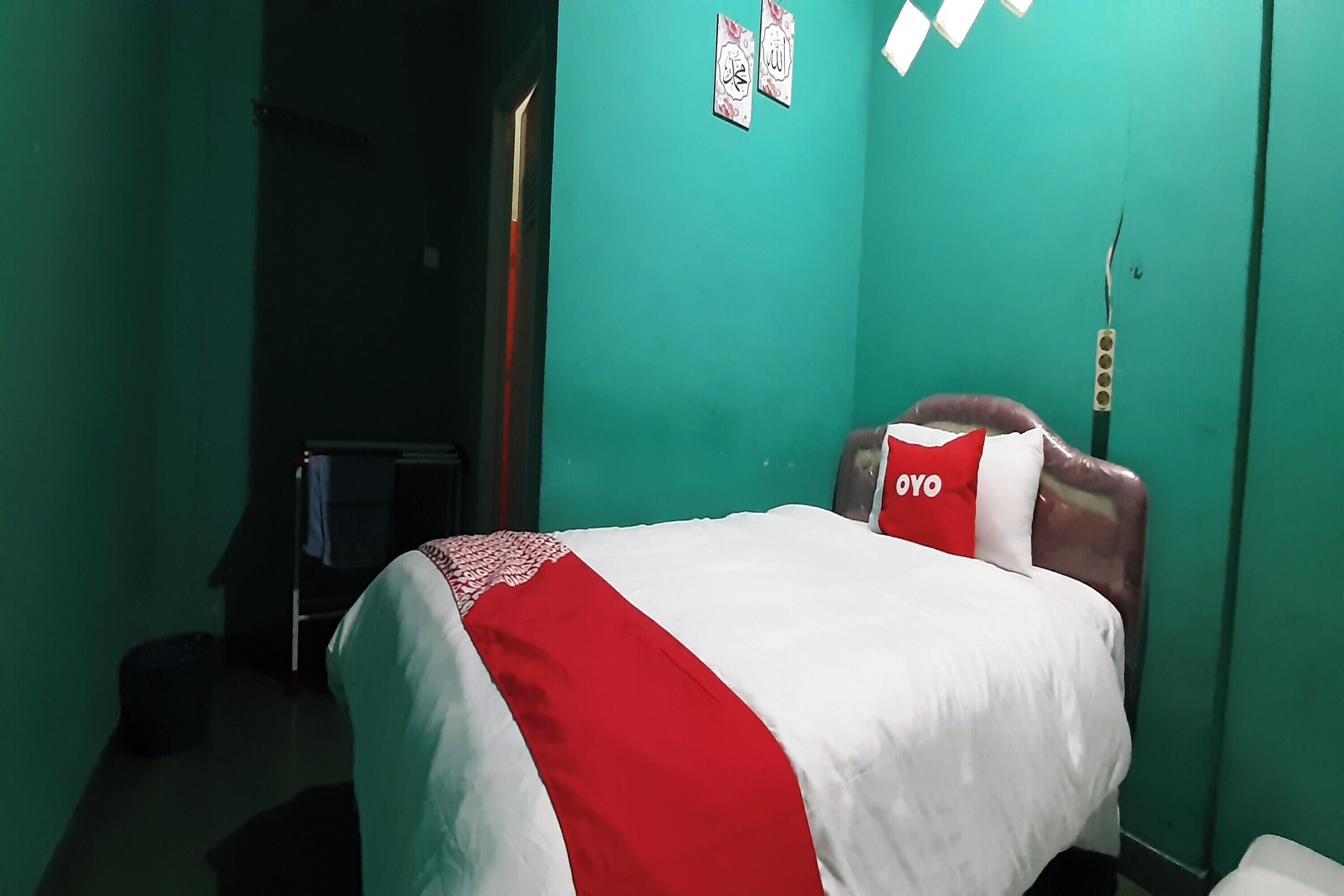 A room with a bed, green walls, and a red and white bedspread.