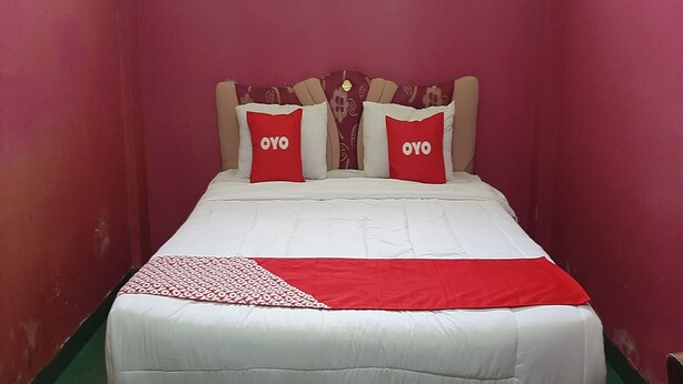 Una cama con una colcha blanca y roja, dos almohadas rojas con el texto "OYO" y un cabecero con estampado floral.