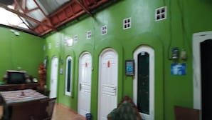 Habitación con paredes verdes, puertas blancas y piso de baldosas. Se observa una mesa con sillas y un televisor.