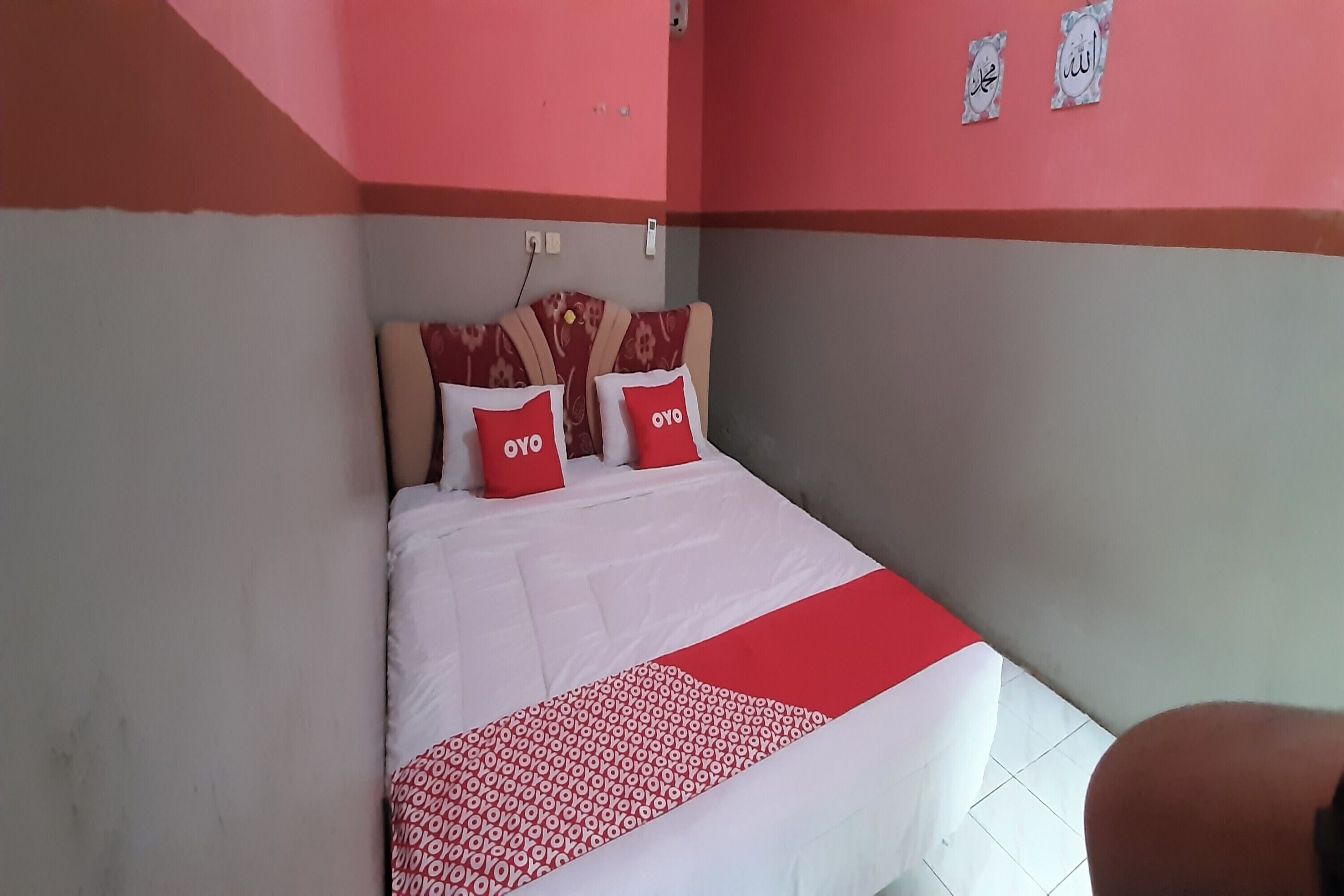 Ein Hotelzimmer mit einem Bett, zwei rote Kissen mit dem Schriftzug "OYO", einer gemusterten Decke und einer rot-weißen Wand.