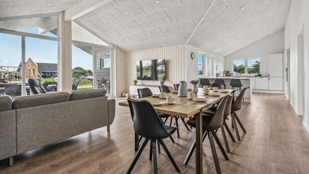 Un grand espace dédié à la salle à manger, avec une longue table en bois, des chaises noires et un canapé gris.