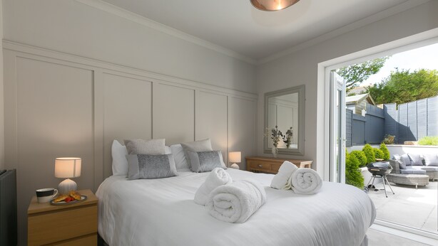 A neatly made bed with rolled towels, a bedside table with a lamp, and a view of the outdoor patio area.